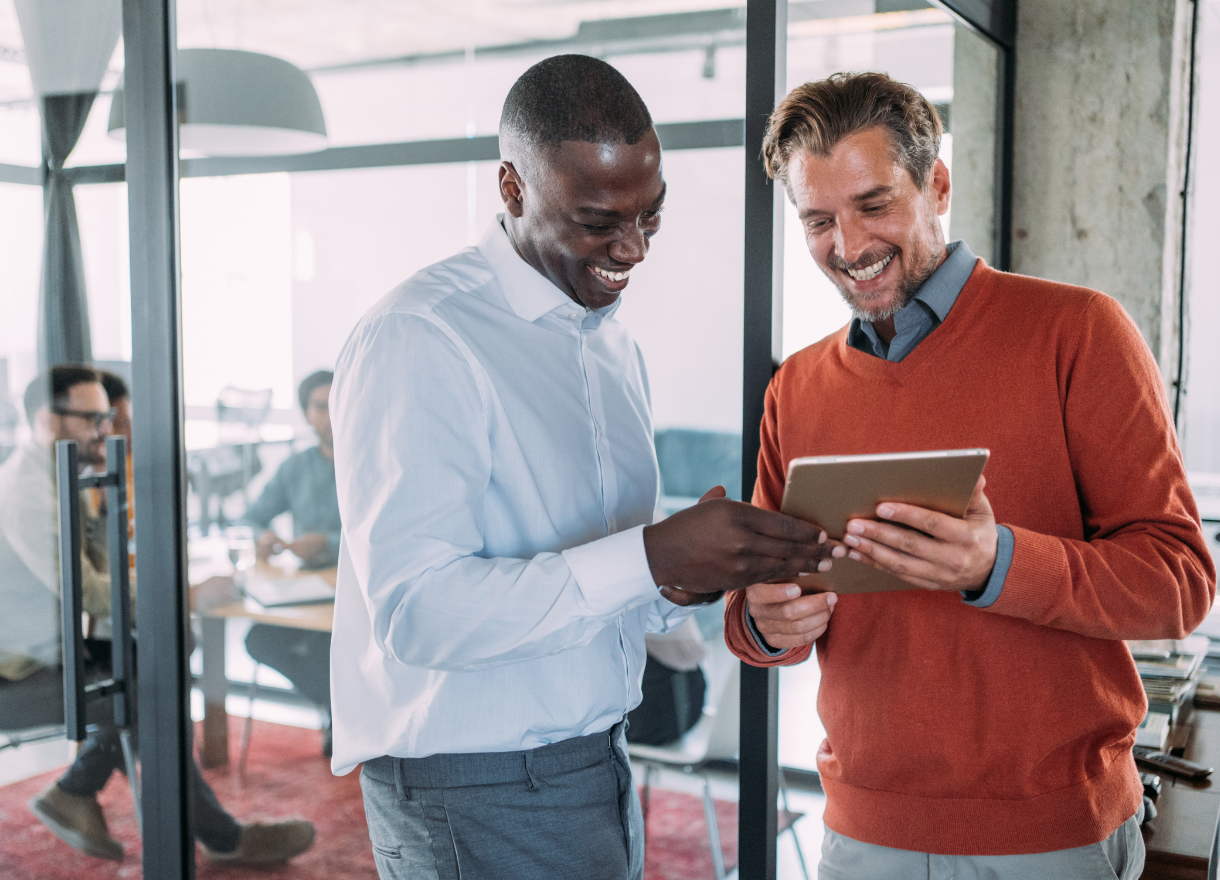 Two colleagues smiling and reviewing work together on a tablet