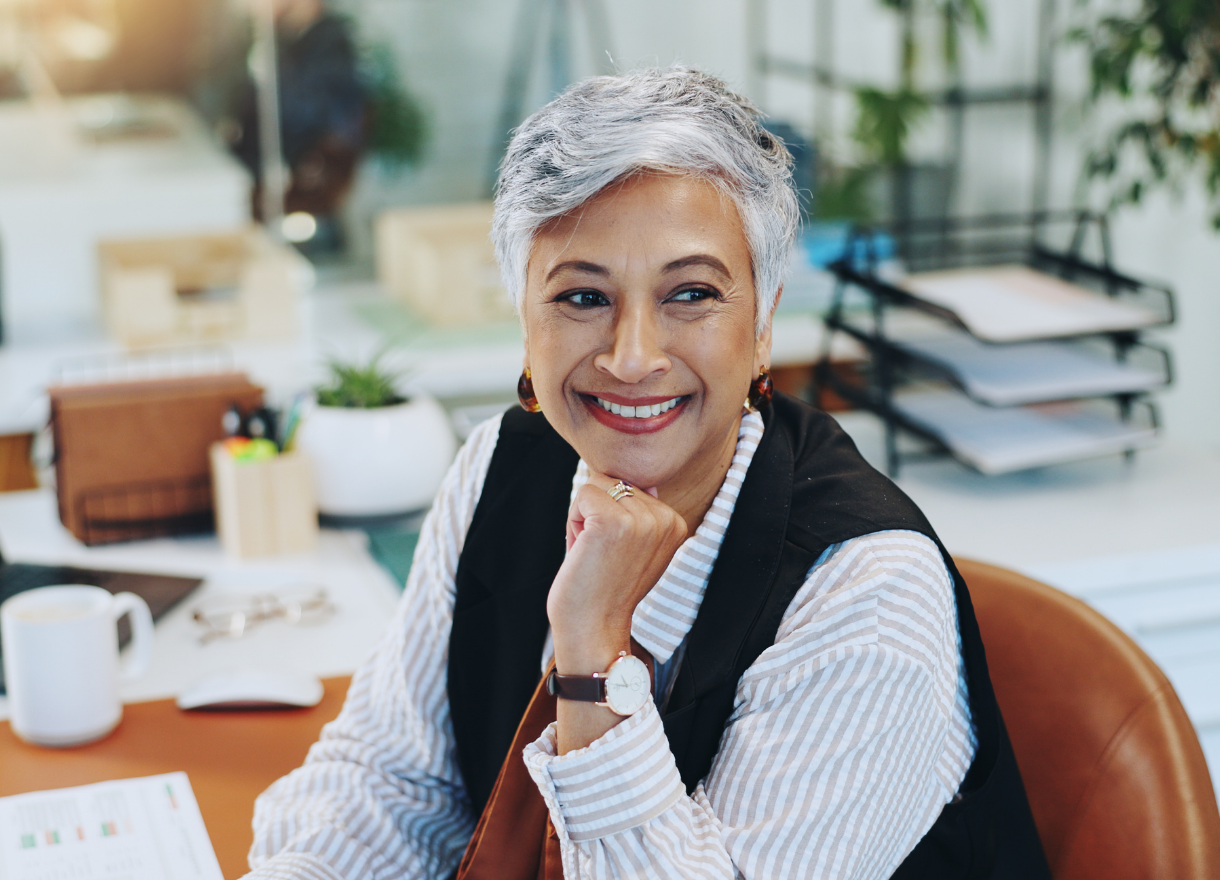 A woman smiling warmly at her desk in a bright workspace