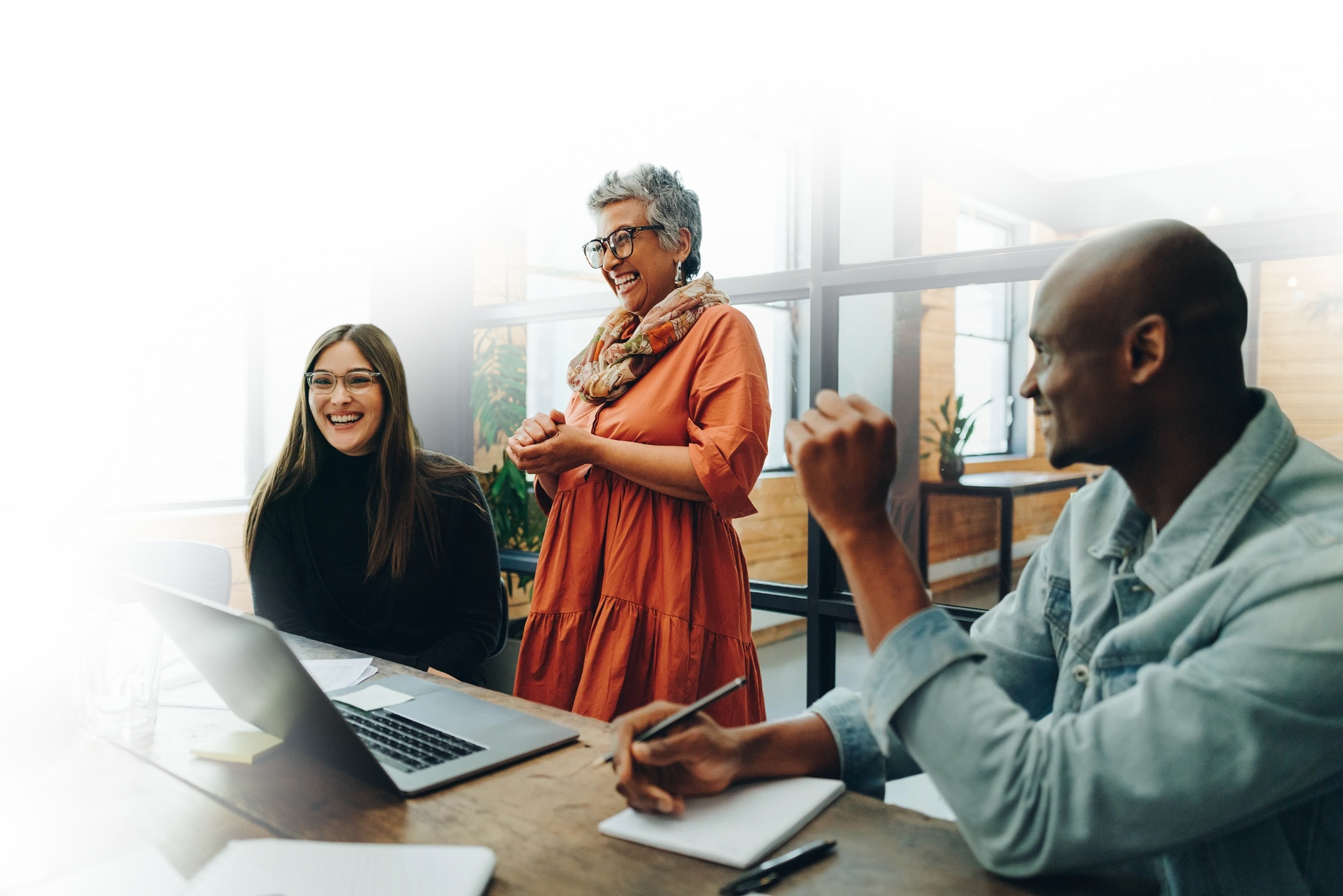 A cross-industry team laughing and working together around a laptop - showcasing AI adoption across roles.